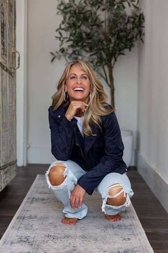 Kim Daly laughing in a navy jacket, crouching in a bright hallway